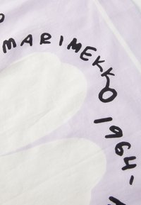 Lila mintázatú textil, amelyen egy nagy fehér virágminta található, merész fekete felirattal, amely tartalmazza a "Marimekko" szót és az "1964" évet.