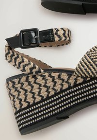 Korkokengät, joissa on kudottu musta ja beige muotoilu, teksturoitu hihna ja musta nahkahakas. Musta pohja geometrisilla kuvioilla.