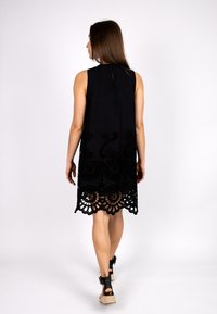 Schwarzes ärmelloses Kleid mit aufwendiger Spitzenverzierung am Saum. Das Design weist florale und geschwungene Muster auf und besteht aus leichtem Stoff.