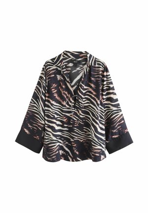 Chemise rayée noir et blanc avec fermeture à liens, coupe ample et manches longues. Présente des poignets noirs unis contrastants. Texture du tissu lisse.