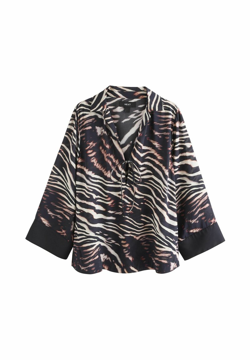 Chemise rayée noir et blanc avec fermeture à liens, coupe ample et manches longues. Présente des poignets noirs unis contrastants. Texture du tissu lisse.
