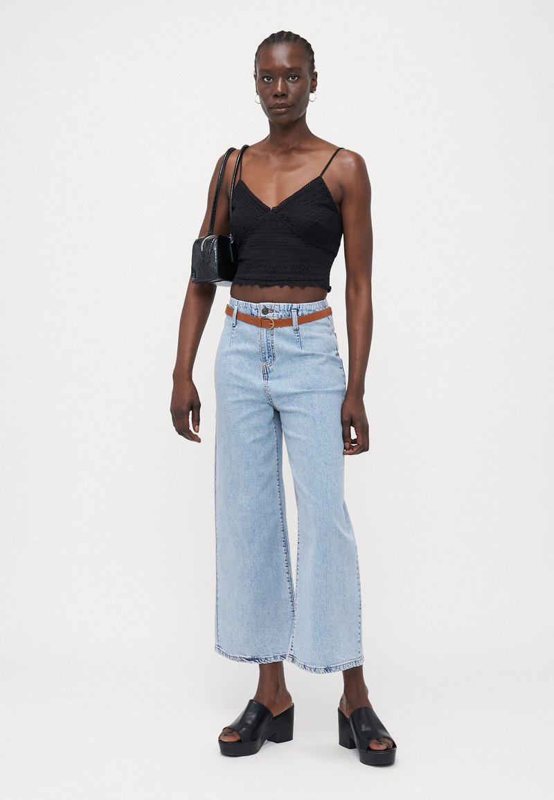 Top corto nero con design texture, jeans a gamba larga azzurri, cintura marrone e zoccoli in piattaforma neri. Borsa nera semplice.