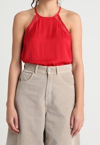 Top a fascetta rossa con dettagli in pizzo, abbinato a pantaloni in corda beige a vita alta con tasche frontali e chiusura a bottone.