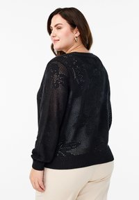 Črn pleten pulover z cvetličnim motivom, zrnato odprto pletenje ter rebrastimi manšetami in spodnjim robom. Odlikuje ga sproščen kroj in okroglo izrezano ovratnik.