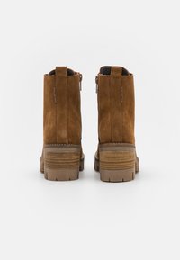 Botines de ante marrón con tacón apilado, cierre de cremallera lateral y lengüeta trasera. Presentan una suela texturizada para mayor agarre.