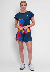 Top deportivo navy con patrones geométricos coloridos en rojo, amarillo y azul; combinado con pantalones cortos a juego. Presenta un cuello redondo y mangas cortas.