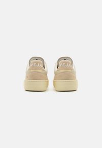 Beige semsket og kremfarget lær sneakers med flate snører, polstret krage og hvit "VEJA" logo på hælen. Gummisåle og teksturerte detaljer.
