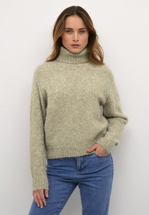 Svijetlozelena, teksturirana turtleneck majica s rebrastim manžetama i porubom, u kombinaciji s plavim trapericama, na jednostavnoj bijeloj pozadini.