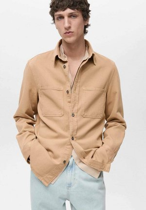 Lichtbruine button-up shirt van katoen, met twee borstzakken, een kraag en een relaxed fit, gedragen over een lichtgekleurde top.
