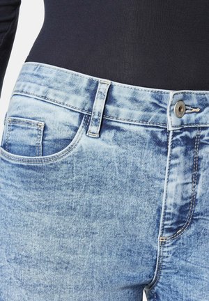Hellblaue Denim-Jeans mit einer ausgewaschenen Textur, ausgestattet mit einer Vordertasche, Gürtelschlaufen und einem metallischen Knopfverschluss an der Taille.