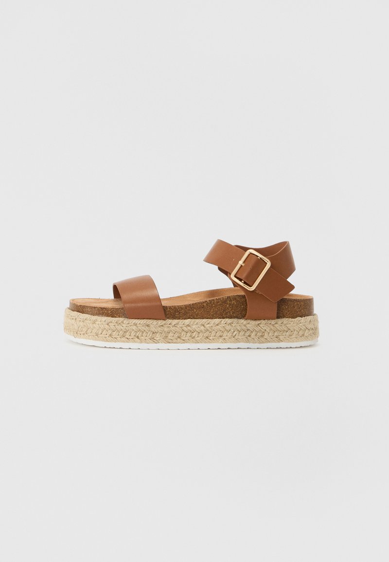 Sandali in pelle marrone con un'unica fascia anteriore e una fascia alla caviglia, con una fibbia dorata e suola platform avvolta in juta.
