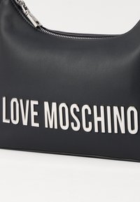 Μαύρη ψεύτικη δερμάτινη τσάντα χεριού με ασημί φερμουάρ και έντονη ασημί επιγραφή "LOVE MOSCHINO" τυπωμένη στο μπροστινό μέρος. Λείο άγγιγμα.