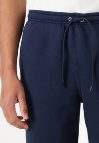 Marinblå mjukisbyxor med elastisk midja och dragsko. Tillverkade av ett mjukt, texturerat tyg. Har en ficka i sidan och en figurnära passform.