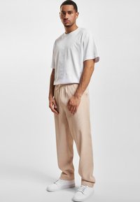Camiseta blanca de manga corta, pantalones de canalé beige y zapatillas blancas. Diseño simple, corte relajado y colores neutros. Sin patrones notables.