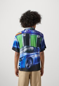 Short-sleeve shirt in a vibrant blue and black design featuring a sports car and green racing numbers. Made of smooth fabric with a relaxed fit.