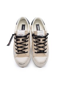 Sneakers in suede beige con lacci neri, un puntale in gomma bianca e dettagli grigi. Presentano un'etichetta con logo e branding sul lato.