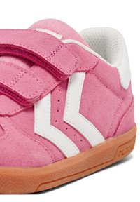 Scarpa in suede rosa con accenti bianchi, dotata di cinturini in Velcro e suola in gomma marrone. Fodera in tessuto e perforazioni sulla tomaia.