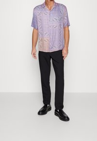 Košile s krátkým rukávem s designem krajky v lila a růžové barvě. V kombinaci s černými kalhotami a lesklými černými botami.