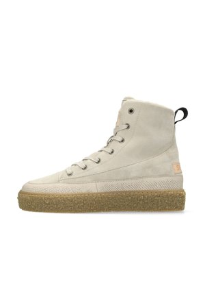 Zapatilla beige de ante de caña alta con cordones en la parte delantera, suela de goma texturizada y lengüeta negra en el talón sobre fondo blanco.