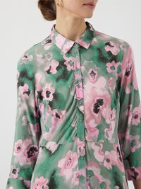 Chemise florale de couleur vert clair avec des motifs de fleurs roses et noires. Caractéristiques d'un col pointu, d'une fermeture à boutons et d'une texture douce et lisse.