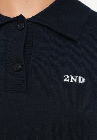 Sötét tengerészkék póló rugalmas gallérral, háromgombos sliccel és fehér hímzett "2ND" logóval a mellkason. Texturált kötött szövet.