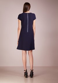 Mörkblå klänning med strukturerad tyg, korta ärmar och dragkedja i mitten av ryggen. Matchad med svarta klacksandaler med ankelremmar.