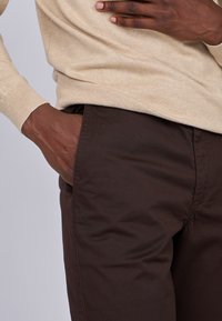 Des poignets de pull en tricot beige et un pantalon en tissu marron avec une poche latérale, montrant une texture lisse et des plis subtils.