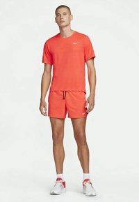 Sarkanais sporta T-krekls un šortu komplekts, izgatavots no viegla auduma. Ietver apļa kakla piegriezumu, brīvu piegriezumu un mazu logo akcentu uz krekla.