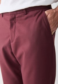 Burgundy trousers in smooth fabric, featuring a flat front, side pockets, and a tailored fit. Clean lines with a polished appearance.