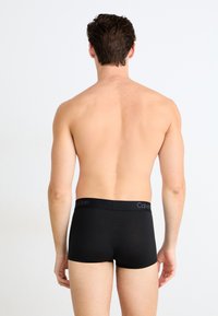 Boxer-briefs noirs en tissu lisse, dotés d'une ceinture douce avec le logo "Calvin Klein". Modèle vu de dos.