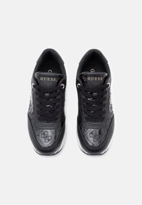 Baskets en cuir noir avec un motif texturé, lacets noirs et logo doré "Guess" sur la langue. Bout arrondi et semelle rembourrée.