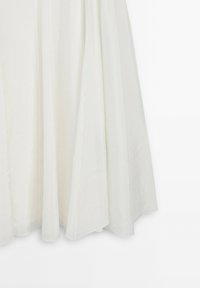Tissu blanc fluide avec de doux drapés et une texture subtile, montrant la partie inférieure d'une jupe ou d'une robe sur un fond blanc uni.