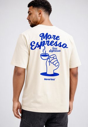 Mann, von hinten gesehen, trägt ein beiges Shirt mit blauem Text "Mehr Espresso weniger Depresso" und eine Hand, die eine dampfende Kaffeetasssen-Illustration hält.