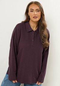 Polo shirt met lange mouwen in donkerpaars geribbeld stof; beschikt over een kraag, knoopsluiting en zijwaarts split voor extra bewegingsvrijheid.