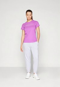 Μωβ κοντομάνικη μπλούζα με λευκό κείμενο, σετ με ανοιχτό γκρι φόρμα και λευκά αθλητικά παπούτσια. Απλό και καθημερινό ντύσιμο.