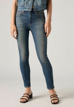 Smarte, mørkeblå denim skinny jeans med subtilt falmning, høj talje, fem lommer og tætsiddende pasform, parret med sorte sandaler med blokhæl.
