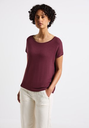 Top corto bordeaux con scollatura ampia, realizzato in tessuto morbido. Abbinato a pantaloni a gamba larga di colore crema con tasche laterali.