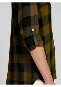 Chemise à carreaux verte et marron avec manches retroussées, dotée d'une fermeture à boutons sur le poignet. Confectionnée dans un tissu doux et texturé, avec une coupe ample.