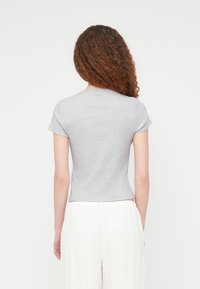 Γκρι κοντομάνικο εφαρμοστό μπλουζάκι με στρογγυλή λαιμόκοψη και λείο ύφασμα, συνδυασμένο με ανοιχτόχρωμο, αέρινο παντελόνι.