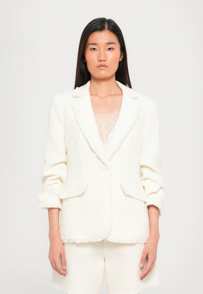 Witte, textuur blazer met rafelige randen, sluiting met één knop en twee voorkruiszakken; gecombineerd met witte shorts.