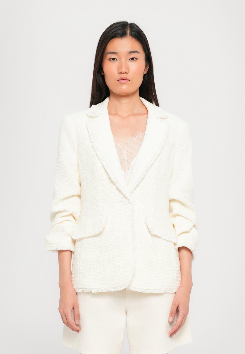 Witte, textuur blazer met rafelige randen, sluiting met één knop en twee voorkruiszakken; gecombineerd met witte shorts.