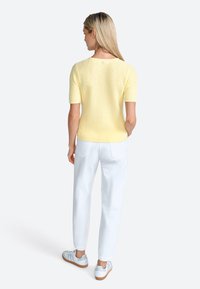 Maglione a maniche corte giallo in maglia con un motivo testurizzato, abbinato a pantaloni bianchi e sneaker azzurri chiari, visto da dietro.