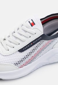 Bílé atletické tenisky s mesh svrškem, kontrastními červenými a námořnickými pruhy a černým akcentem s logem "TOMMY HILFIGER" na boku.
