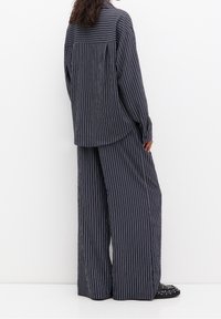 Chemise oversize rayée verticale bleu marine et pantalon large en tissu léger. Pr ésente une coupe lâche et une texture subtile.