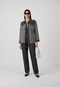 Čierno-biela houndstooth bunda s deninovými akcentmi, čierne kožené nohavice a malá levanduľová kabelka, doplnené čiernymi slnečnými okuliarmi.