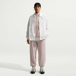 Kvinde iført en hvid lynlåsjakke over en lys pink sweatshirt og matchende joggingbukser, stående foran en ensfarvet hvid baggrund.