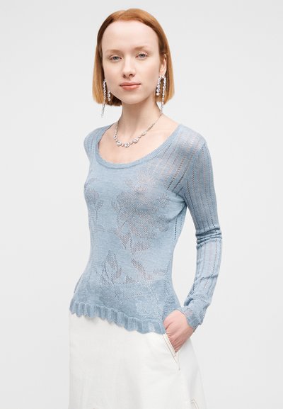 Pull tricoté bleu clair avec motifs floraux, encolure côtelée et ourlet festonné. Manches longues et coupe légèrement ajustée.