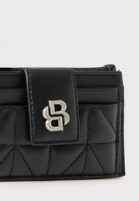 Fekete bőrpénztárca steppelt mintával, ezüst logós díszítéssel és patentzáras rögzítéssel. Vízszintes kártyatartó rekeszekkel és texturált felülettel rendelkezik.