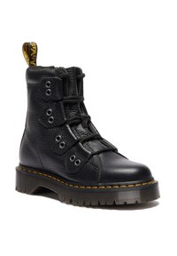 Botte à cheville en cuir noir avec une semelle épaisse, des coutures jaunes et un laçage unique traversant trois panneaux à œillets, avec une languette de tirage marquée.