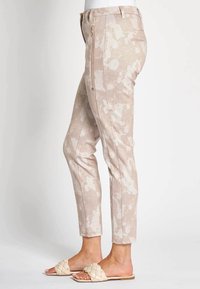 Beige patterned pants with a slim fit, featuring a side zip pocket and solid waistband. Worn with light-colored flat sandals.